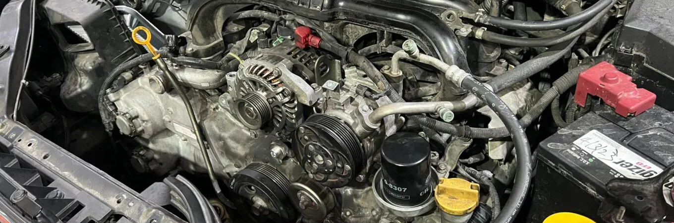 Detailed view of a car engine bay showing alternator, belts, and battery during maintenance