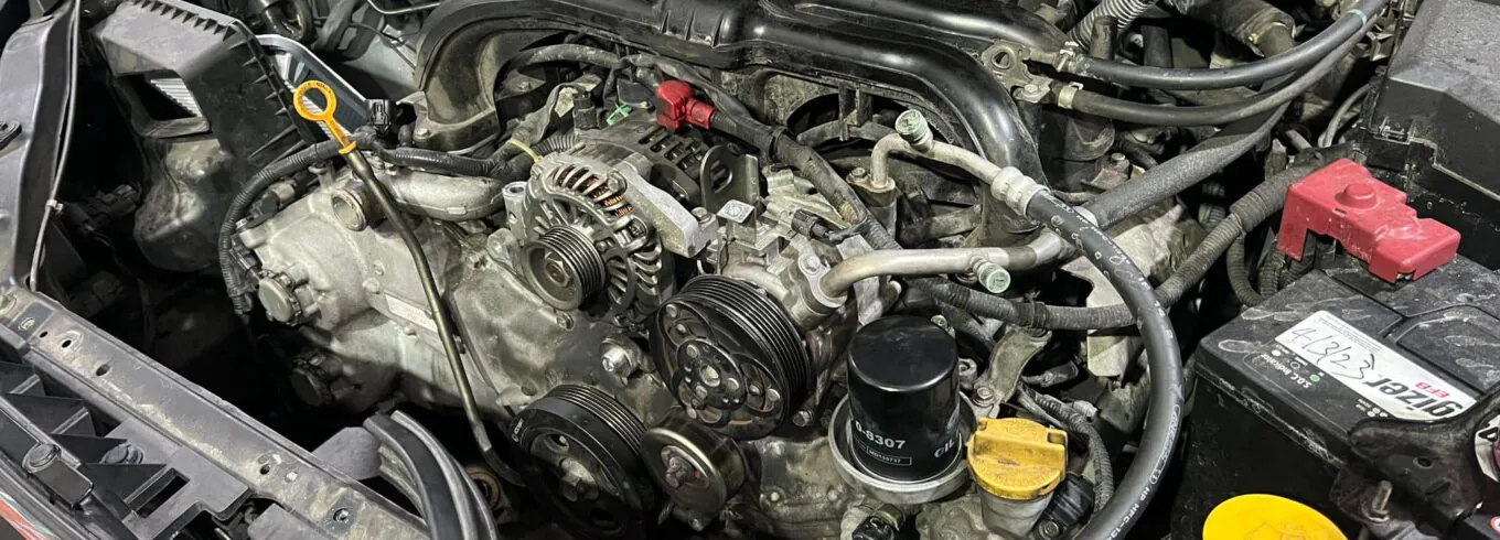 Detailed view of a car engine bay showing alternator, belts, and battery during maintenance