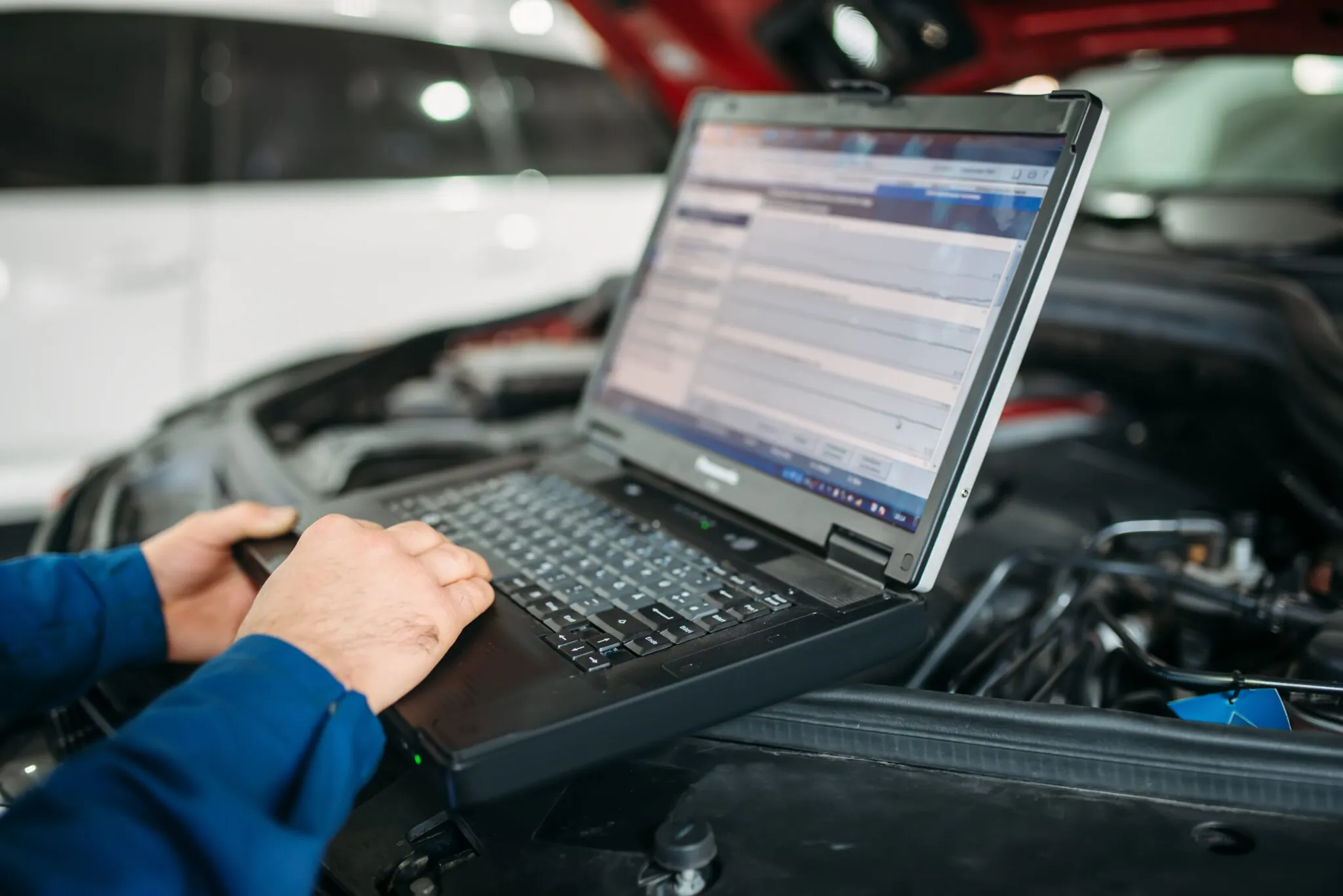 Mechanic performing car diagnostics with laptop connected to engine